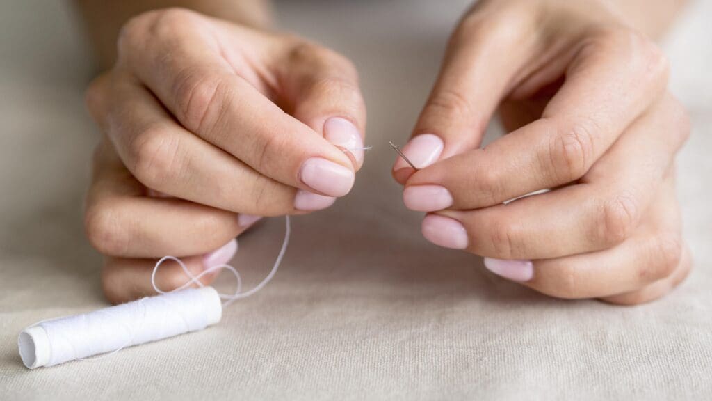 Hands threading a needle with white thread