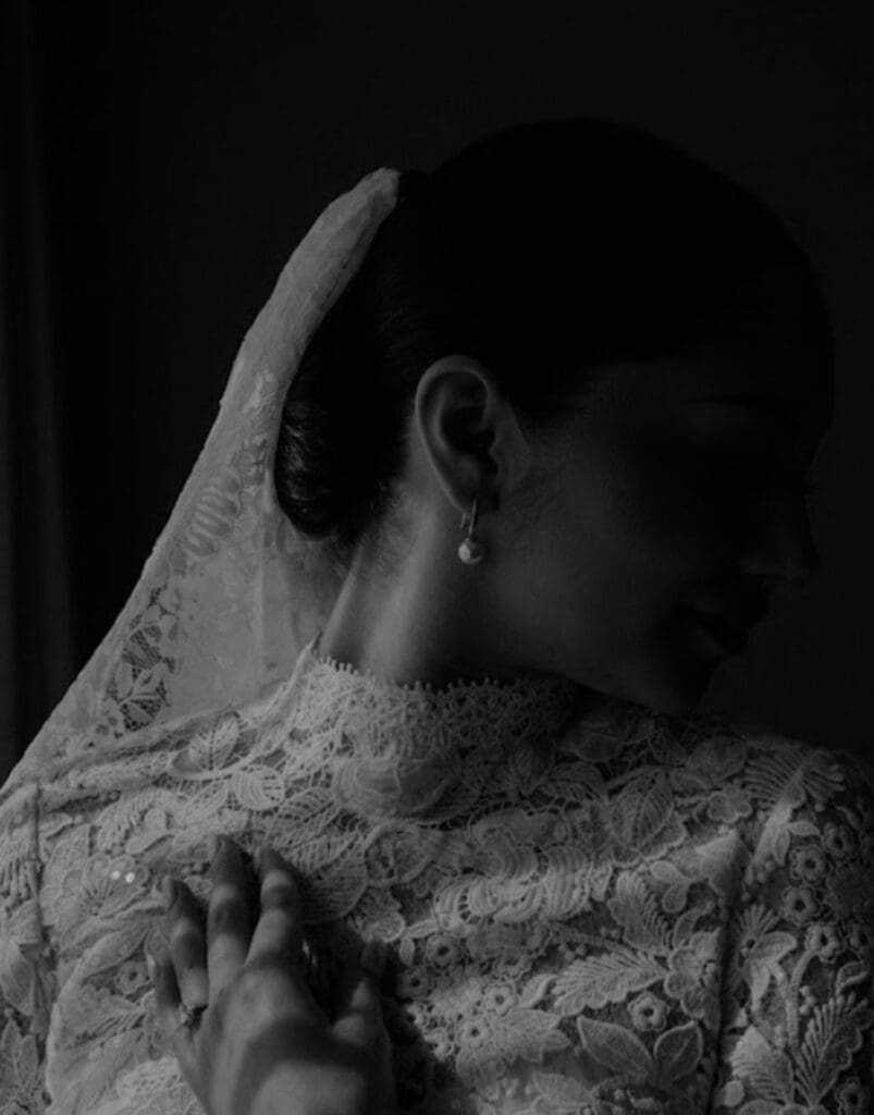 Close-up of a bride in a lace high-neck wedding gown with delicate floral details, wearing a pearl earring and veil