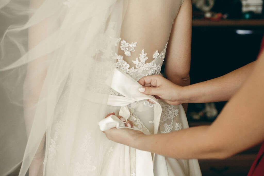 Bride’s lace dress being tied with satin ribbon at waist