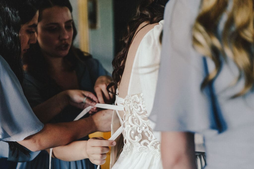 Bridesmaids fastening corset back of wedding gown